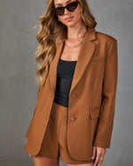 Woman wearing camel brown blazer and matching shorts set with black tube top, gold chain necklaces, and cat-eye sunglasses
