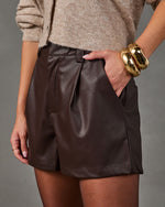 Brown faux leather pleated shorts styled with a beige knit cardigan, sheer tights and chunky gold bangle bracelets