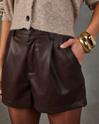 Brown faux leather pleated shorts with belt loops styled with a beige knit cardigan and chunky gold bangle bracelets