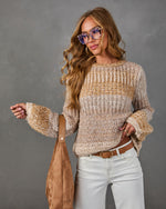 Woman wearing a chunky beige and camel knit sweater with white jeans, tan belt, tortoiseshell glasses and suede hobo bag