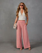 Woman wearing pink wide-leg palazzo pants with white ribbed halter crop top, gold accessories, and strappy sandals