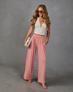 Woman wearing pink wide-leg pleated pants and cream halter crop top with strappy heels and woven clutch