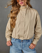 Woman wearing khaki cropped bomber jacket with mock neck and elastic hem, paired with light wash wide-leg jeans