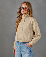 Woman wearing khaki zip-up bomber jacket and light wash jeans with aviator sunglasses and gold hoop earrings