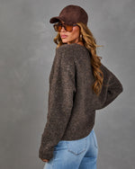 Woman in brown suede cap and tinted sunglasses wearing a oversized brown boucle sweater and light wash jeans, back view
