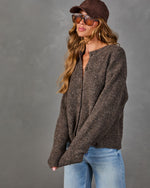 Woman in a brown boucle button-front cardigan, suede baseball cap, tinted aviator sunglasses and light wash wide-leg jeans
