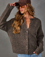 Woman wearing a brown textured boucle button-front cardigan with a suede cap, tinted aviator sunglasses and light-wash jeans