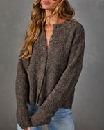 Brown textured boucle cardigan with button front and oversized sleeves, styled with light wash jeans and gold hoop earrings