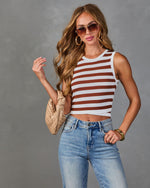 Woman wearing brown and white striped crop tank top with high-waist jeans, woven bag, gold hoops, and aviator sunglasses