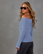Woman in a blue and black striped off-the-shoulder foldover sweater with dark wide-leg jeans, sunglasses and gold hoop earrings