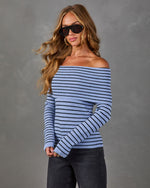 Woman wearing a blue and black striped off-the-shoulder knit sweater with dark gray jeans, hoop earrings and black sunglasses