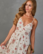 Woman wearing cream floral maxi dress with pink roses, spaghetti straps, V-neckline, gold jewelry, wicker clutch