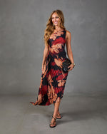 Woman wearing black and red floral pleated midi dress, black strappy heels, and small black handbag, smiling confidently