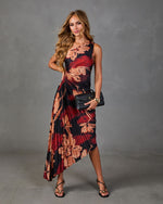 Woman wearing black floral pleated midi dress with red blooms, black strappy heels, and woven clutch bag