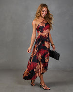Woman wearing black floral pleated one-shoulder midi dress with red print, black heeled sandals, and clutch bag