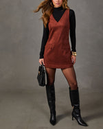 Rust suede V-neck mini dress over black mock-neck top with black knee-high stiletto boots, sheer tights and woven handbag