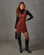 Woman wearing a rust suede V-neck mini dress over a black turtleneck with black knee-high boots and a woven black handbag