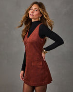 Woman in a rust brown suede V-neck mini dress with flap pocket, layered over a black mock neck top and sheer tights