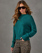 Woman wearing a teal green mock neck cropped sweater with ribbed hem and cuffs, styled with leopard print jeans and aviator sunglasses