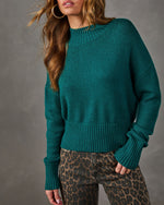 Teal green mock neck knit sweater with ribbed hem and cuffs, styled with leopard print jeans and gold hoop earrings