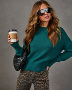 Woman in a teal mock neck knit sweater, leopard print jeans, black woven bag and sunglasses holding a takeaway coffee cup