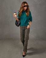 Woman in emerald green knit sweater, leopard print jeans, black pumps and woven bag holding a coffee cup, fall outfit
