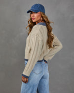 Woman in a cream ribbed knit cropped sweater with blue trim, denim baseball cap and light wash high-waisted jeans