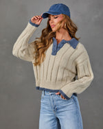 Woman wearing a cream ribbed knit polo sweater with blue collar trim, a blue baseball cap, and light wash high-rise jeans