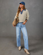 Woman in cream ribbed polo sweater with blue collar, light wash wide-leg jeans, denim cap, and beige western ankle boots