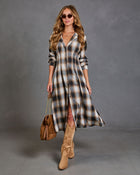 A woman models a long-sleeve plaid midi shirt dress in brown, beige, and white tones, styled with tan suede knee-high boots, a brown leather handbag, and sunglasses against a textured gray studio background.