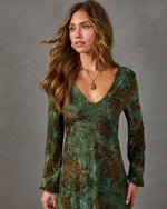 Woman in a green long-sleeve V-neck midi dress with brown rose print, paired with a gold pendant necklace and hoop earrings