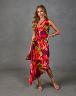 Woman wearing bold tropical floral pleated midi dress in red and purple, styled with gold earrings and nude strappy heels