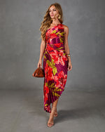Woman wearing bold tropical floral pleated midi dress in magenta and red with asymmetric hem, gold accessories, nude strappy heels