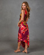 Woman modeling backless tropical floral pleated midi dress in magenta and red with strappy nude heels and gold accessories