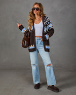 Woman wearing brown and blue Fair Isle cardigan, white crop top, distressed light-wash jeans, and brown platform slippers
