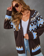Brown Fair Isle cardigan with blue and gold patterns, styled with white tank, light wash jeans, and oversized sunglasses