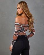 Woman wearing brown floral off-shoulder mesh long-sleeve bodysuit with black high-waist jeans, back view