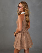 Woman in tan tweed fit-and-flare mini dress with white collar, gold accessories, and aviator sunglasses, smiling over shoulder
