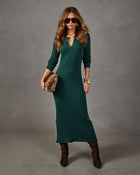 Woman wearing a green ribbed knit midi dress with henley buttons, brown suede boots, sunglasses, and a faux fur clutch