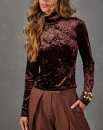 Brown crushed velvet long-sleeve mock neck top styled with wide-leg brown pleated trousers and chunky gold bangles