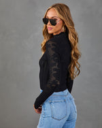 Woman wearing black open-knit crochet sweater and light wash jeans, posed sideways with aviator sunglasses and wavy blonde hair