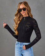Woman wearing black pointelle knit long-sleeve top with open-weave pattern, light wash jeans, gold hoops, and aviator sunglasses