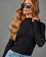 Woman wearing black open-knit pointelle sweater with mock neck and long sleeves, paired with light wash jeans and aviator sunglasses