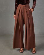 Brown wide-leg pleated trousers with high waist, styled with a burgundy velvet long-sleeve top and strappy heeled sandals