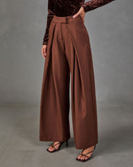 Brown high-waisted wide-leg pleated trousers styled with a burgundy velvet long-sleeve top and strappy block-heel sandals