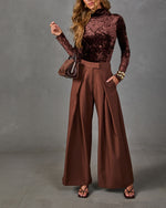 Woman in brown crushed velvet turtleneck and wide-leg pleated chocolate trousers with mini handbag and gold cuff bracelets