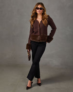 Woman wearing a brown knit cardigan with faux fur trim, black flare pants, brown pumps, sunglasses and a clutch