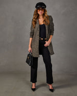 Woman in herringbone tweed coat, black top, wide-leg jeans, baker boy cap, aviator sunglasses, woven handbag and pointed heels