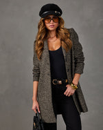 Woman in a herringbone tweed coat, black bodysuit, black jeans, suede newsboy cap, tinted aviator sunglasses and gold bangles