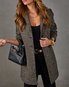 Woman wearing a herringbone tweed blazer coat over black outfit with black woven leather handbag and gold bangle bracelet